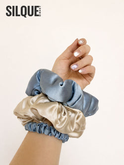 Three mulberry silk scrunchies in dusty blue and champagne beige styled on a wrist